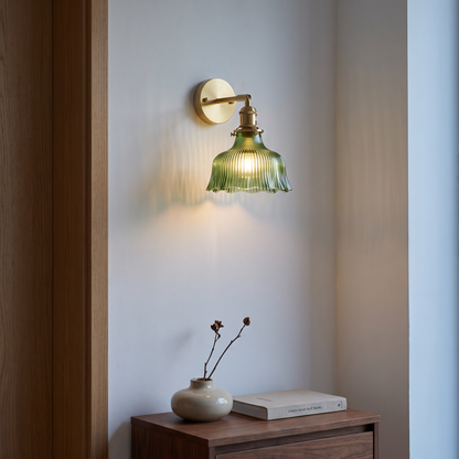 Green glass and brass flower wall sconce lit at dusk above a walnut console in a Nordic living room