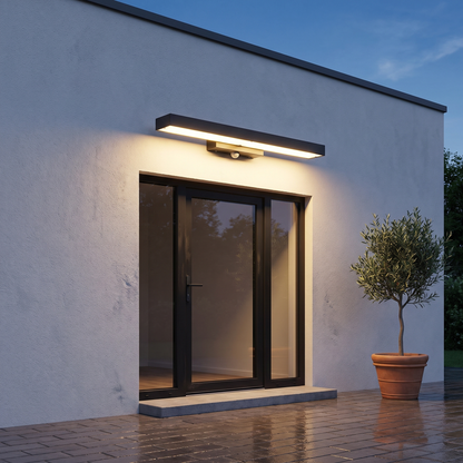 Modern minimalist black rectangular LED outdoor wall sconce lit at dusk above a front door on a white stucco house