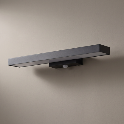 Black flat rectangular waterproof LED sensor outdoor wall light mounted on a plain rendered wall, light off