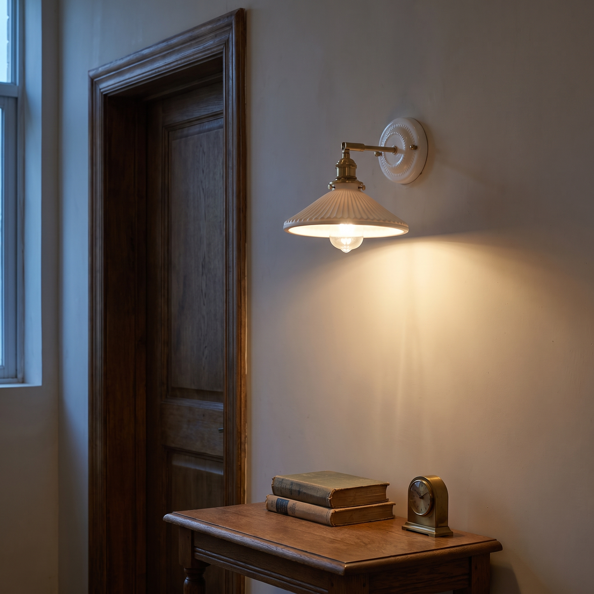 White ceramic brass wall sconce lit at dusk in a vintage hallway beside an oak door frame above a console table