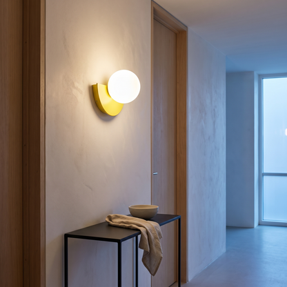 Yellow semicircle glass globe wall sconce lit in a minimalist hallway beside an oak door frame