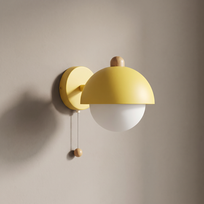 Wheat yellow macaron dome wall sconce with opal glass globe, wood knob and pull cord on a plain greige wall, light off