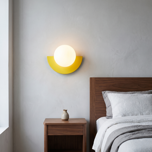 Modern minimalist yellow semicircle glass globe wall sconce glowing warm beside a walnut bed