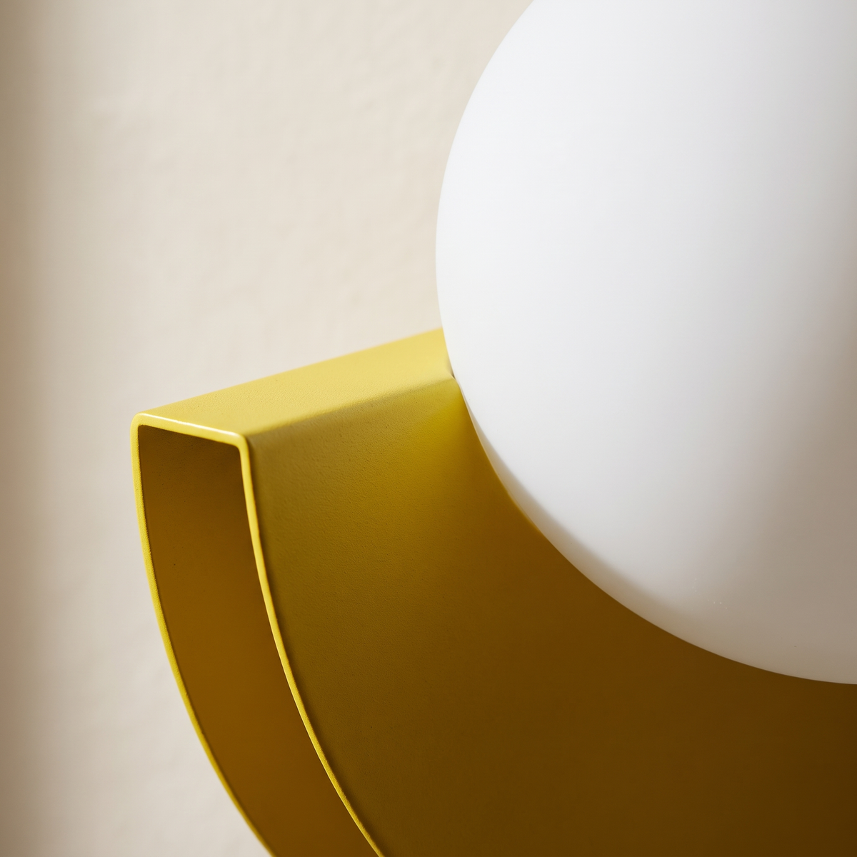 Close-up of the matte yellow powder-coated semicircle and opal glass globe on the modern wall sconce