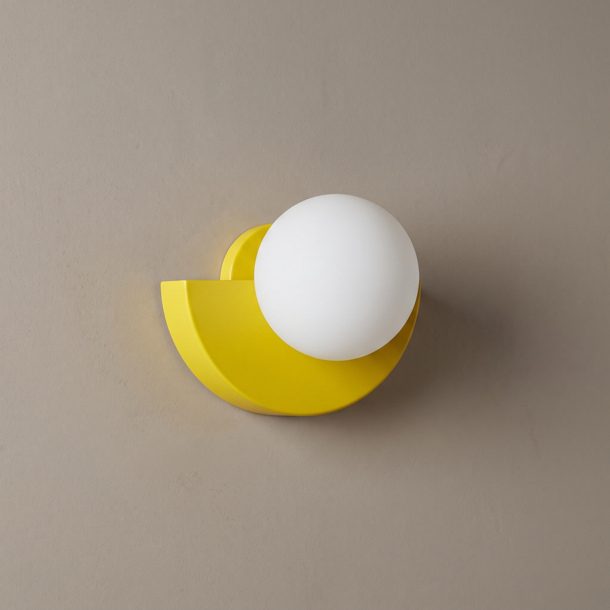Yellow iron semicircle wall sconce with white opal glass globe on a plain greige wall, light off