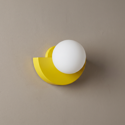 Yellow iron semicircle wall sconce with white opal glass globe on a plain greige wall, light off