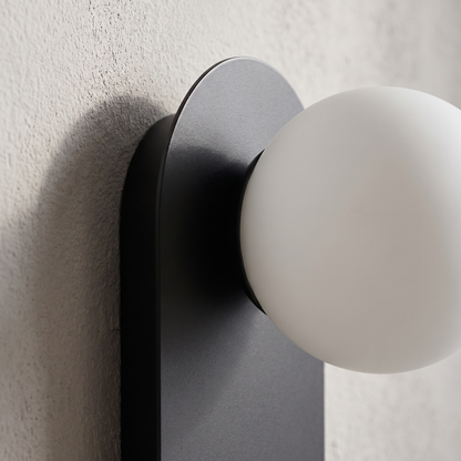 Close-up of the opal glass globe meeting the matte black metal backplate on the minimalist wall sconce