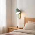 Nordic macaron sage green cylinder rotatable wall sconce glowing warm beside a light oak bed and nightstand