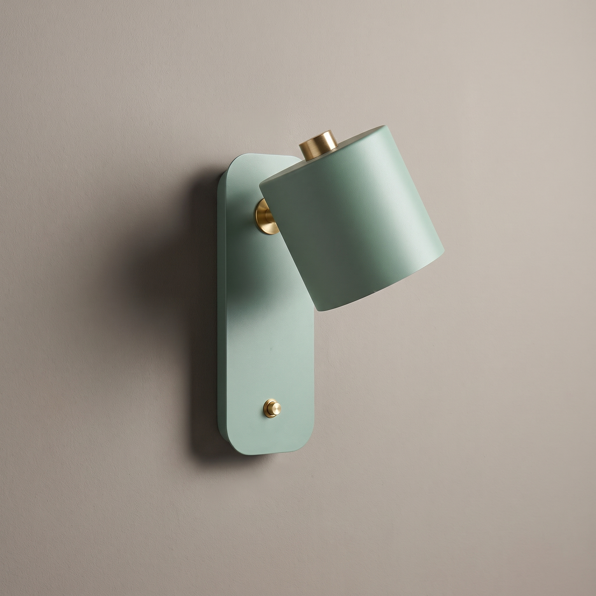 Sage green metal cylinder wall sconce with push button switch and rotatable shade on a plain greige wall, lamp off