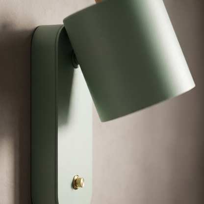 Close-up of the rotatable pivot, matte green powder-coated cylinder and push button of the Nordic macaron wall sconce