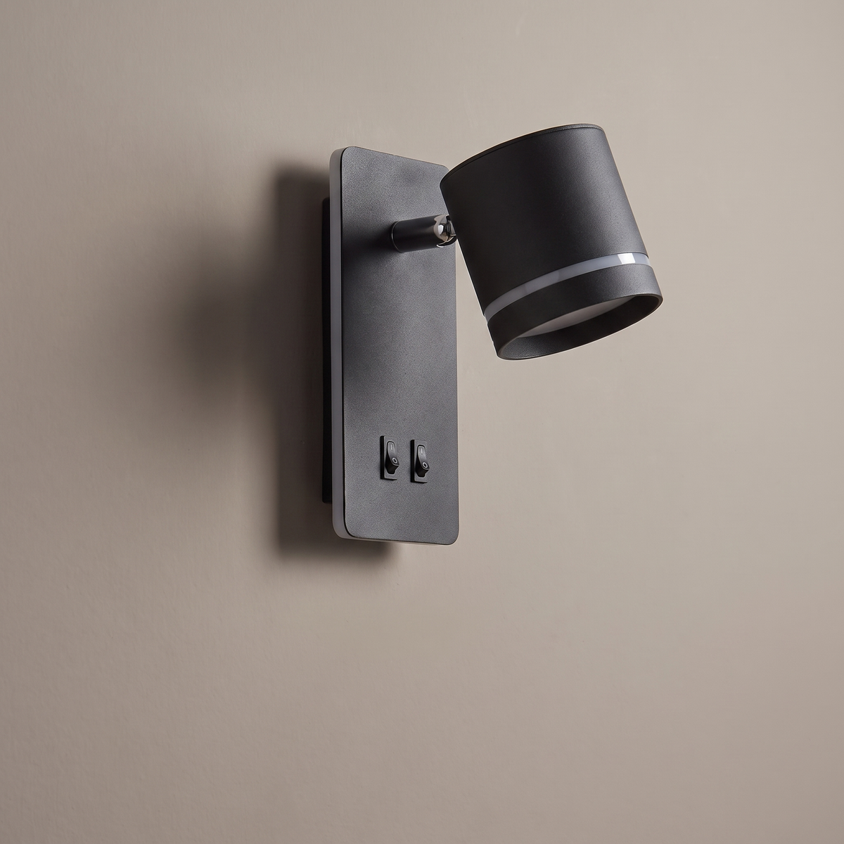 Black iron square backplate wall sconce with rotatable cylinder spotlight and switches on a plaster wall, lamp off