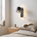 Nordic black iron rotatable LED spotlight reading wall sconce glowing warm beside an oak bed