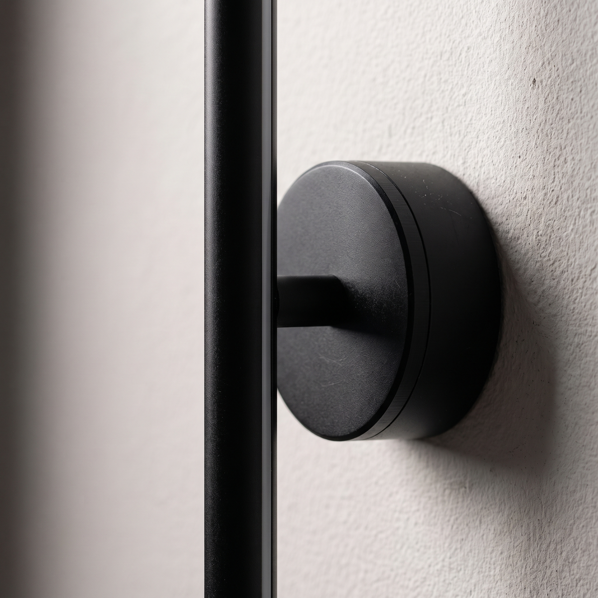 Close-up of the round black mount disc and matte aluminum bar of the minimalist strip LED wall sconce