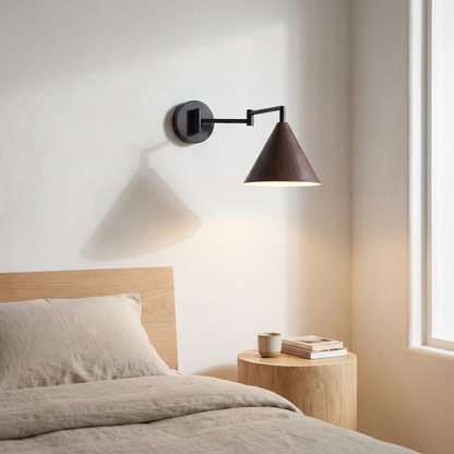 Nordic black iron swing arm wall sconce with walnut wood-grain cone shade glowing warm over an oak nightstand beside a bed