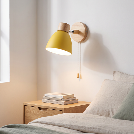 Macaron yellow iron and wood wall sconce with pull cord switch glowing warm beside an oak bed