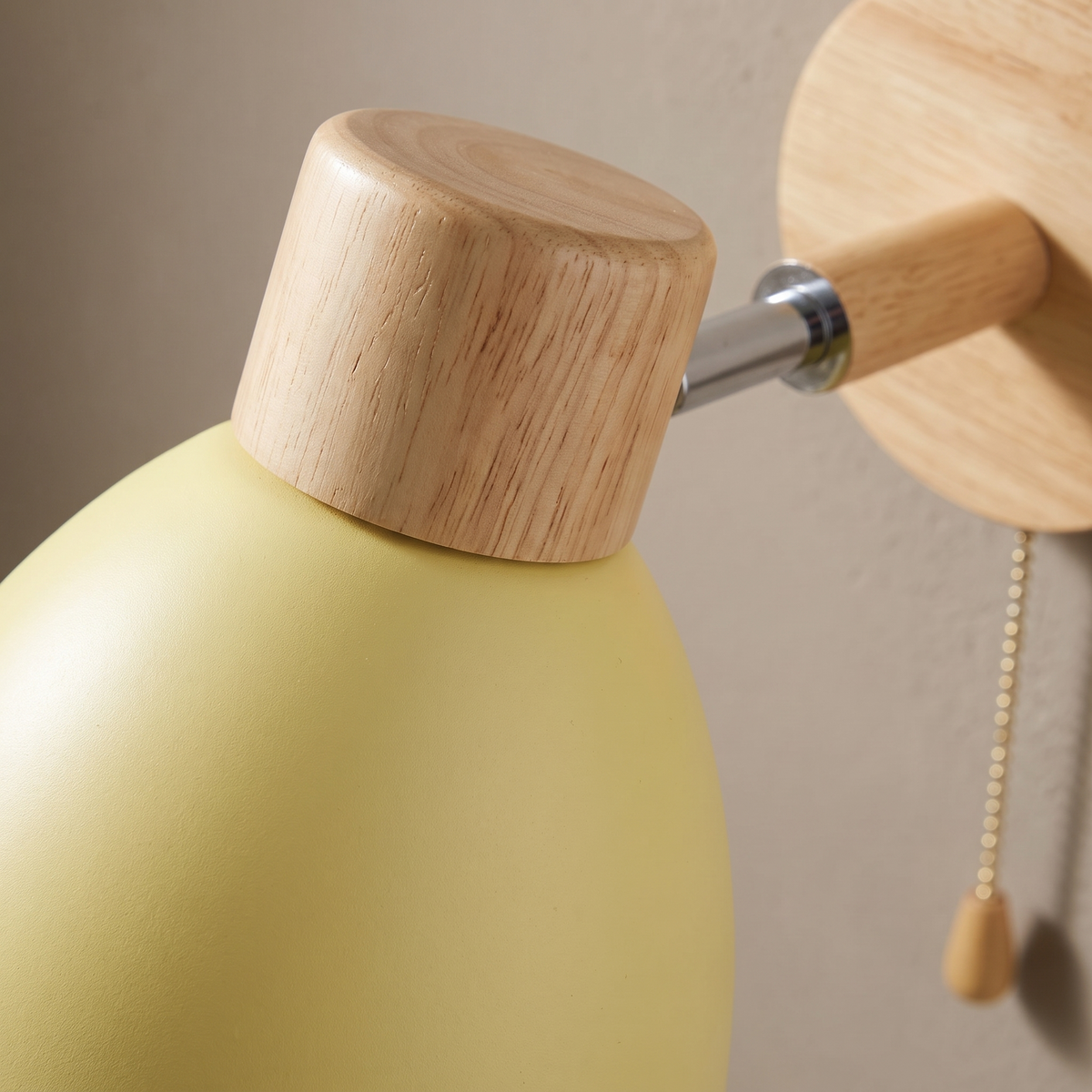 Close-up of the natural wood cap, matte yellow iron shade and pull cord on the macaron wall sconce
