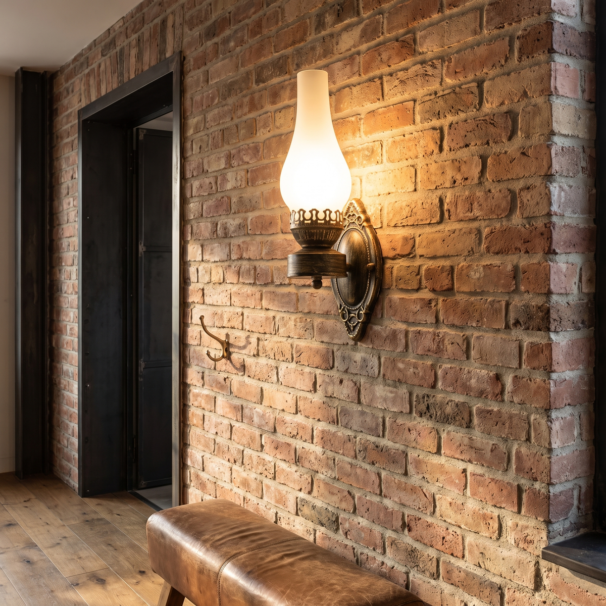 Retro kerosene style antique bronze wall sconce with frosted glass chimney glowing warm on a reclaimed brick hallway wall