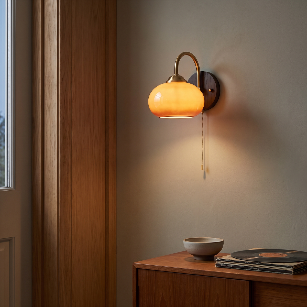 Mid-century caramel glass ash wood wall sconce lit beside an oak door frame above a teak sideboard, showing mounting height and scale