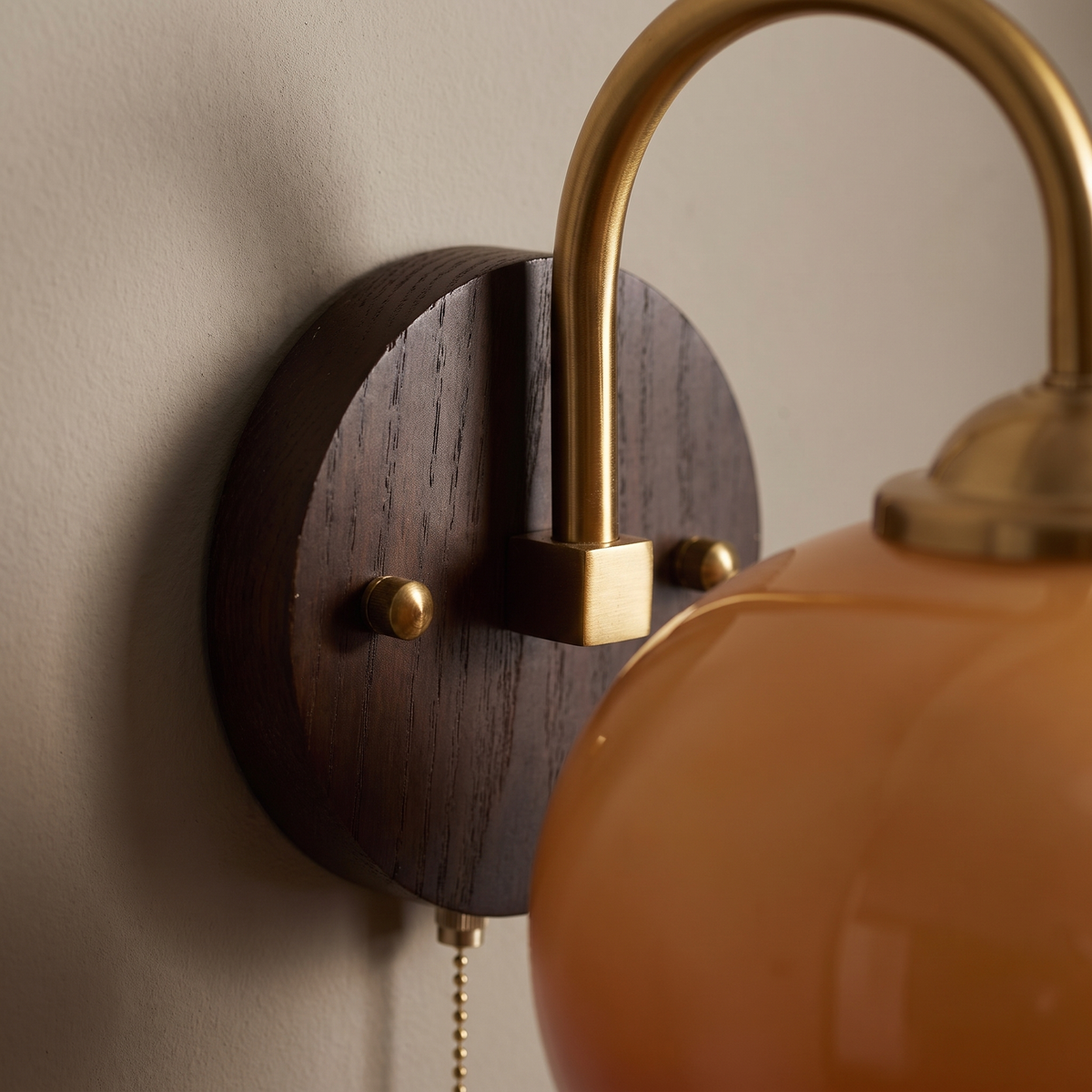 Close-up of the brass gooseneck arm meeting the dark-stained ash wood backplate of the mid-century glass wall sconce