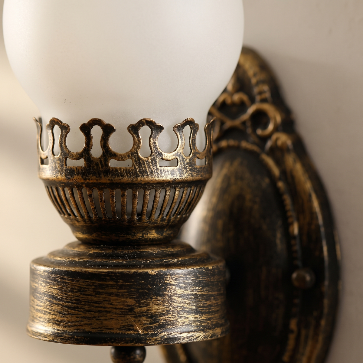 Close-up of the brushed bronze fluted oil font and pierced gallery holding the frosted glass chimney of the retro kerosene wall sconce