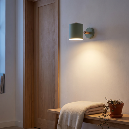 Nordic macaron sage green cylinder wall sconce lit beside an oak door frame above a bench in a Scandinavian reading nook, showing scale