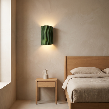Contemporary Nordic green striped resin half cylinder 2-light wall sconce casting an up and down glow beside an oak bed