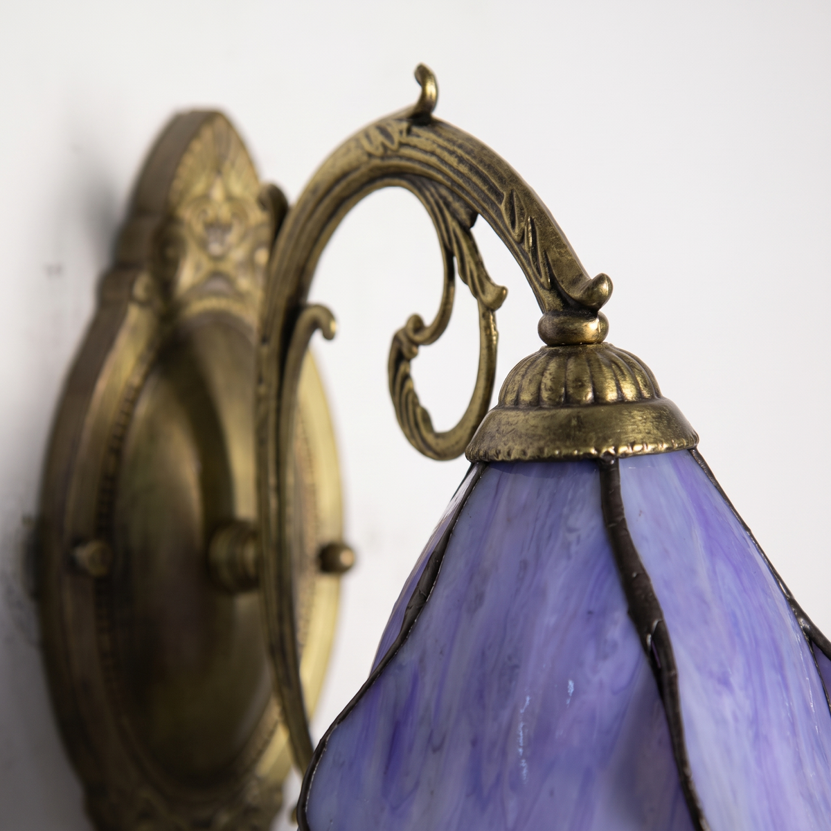 Close-up of the leaded purple stained glass petals and antique bronze scrolled arm of the Tiffany wall sconce