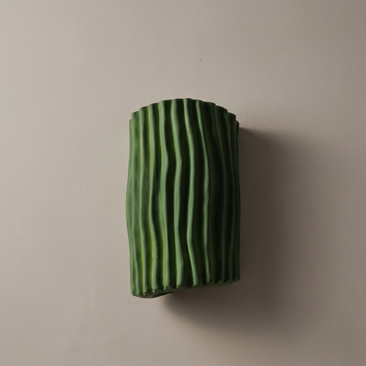 Green fluted resin half cylinder wall sconce, lamp off, mounted on a warm greige plaster wall