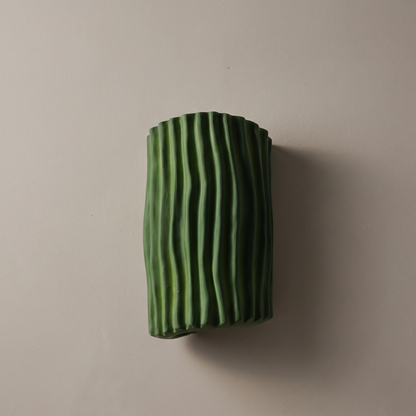 Green fluted resin half cylinder wall sconce, lamp off, mounted on a warm greige plaster wall