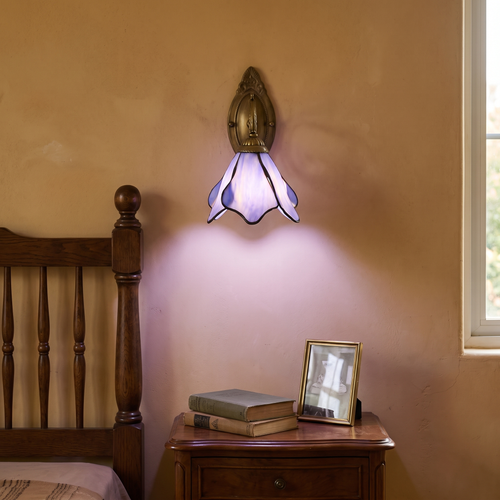 Vintage Tiffany purple stained glass petal wall sconce glowing warm beside a dark oak bed above an antique nightstand