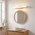 Nordic minimalist wooden long strip LED vanity light glowing warm above a round oak mirror in a Scandinavian bathroom