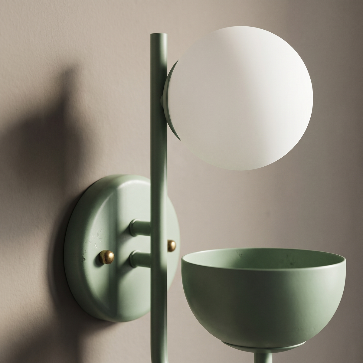 Close-up of the sage green painted iron arm, round backplate and frosted glass globe of the planter wall sconce