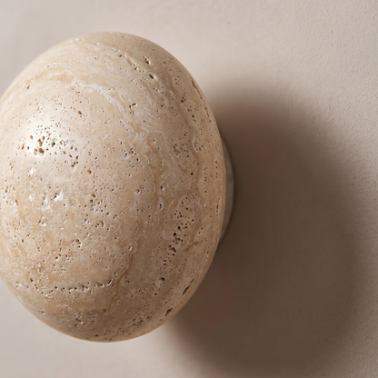 Close-up macro of the honed yellow travertine surface with natural pores and veining on the round wall sconce