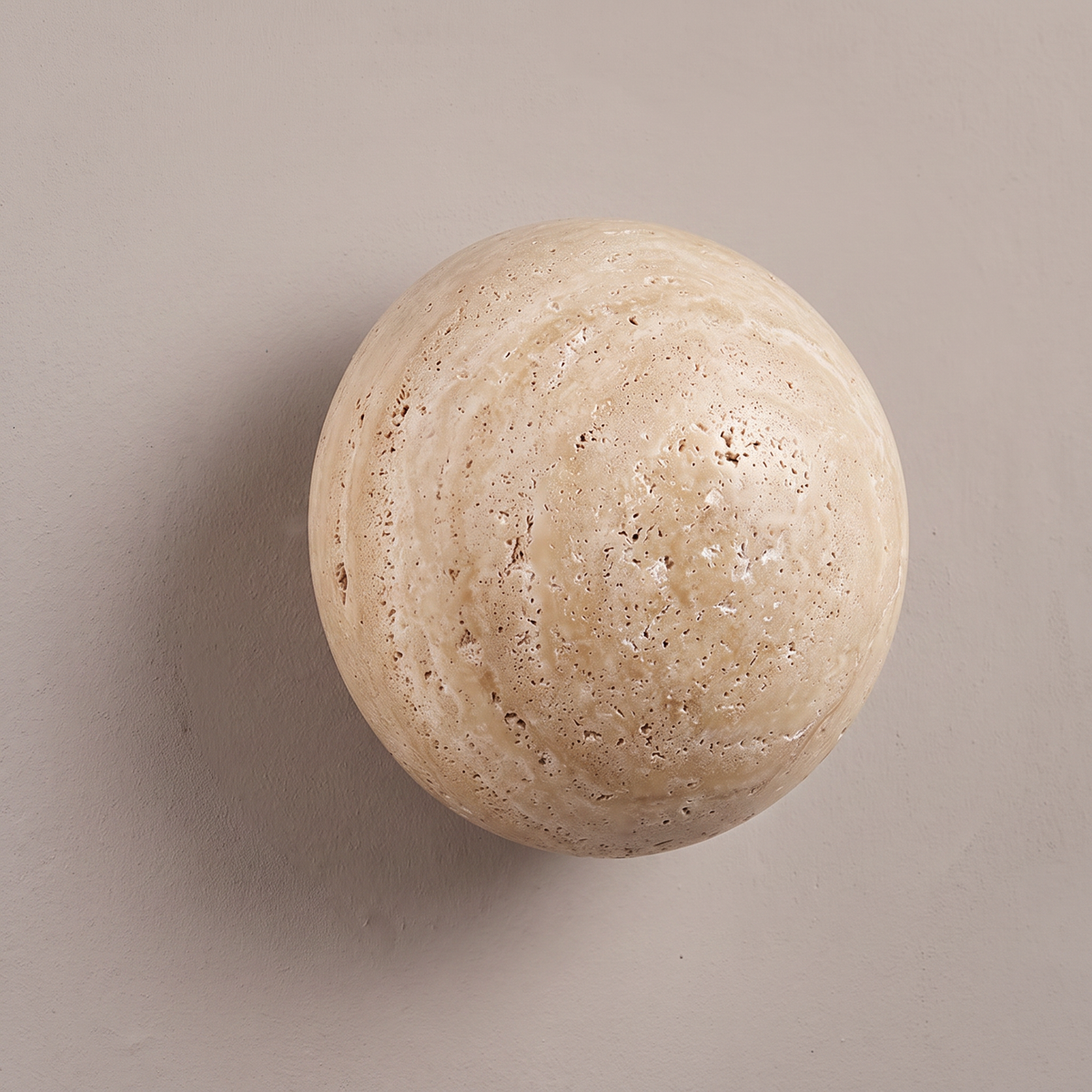 Round yellow travertine stone disc wall sconce on a plain greige plaster wall, lamp off, showing natural pitted texture