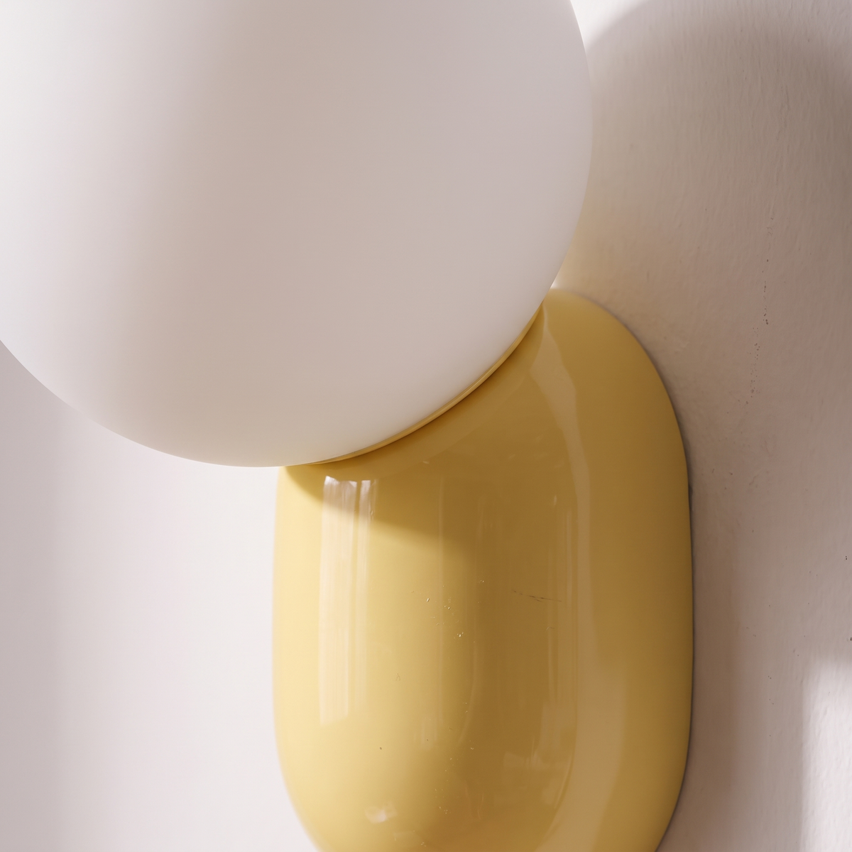 Close-up of the frosted white glass globe resting on the glossy yellow resin base of the macaron wall sconce