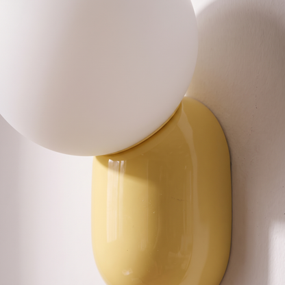Close-up of the frosted white glass globe resting on the glossy yellow resin base of the macaron wall sconce