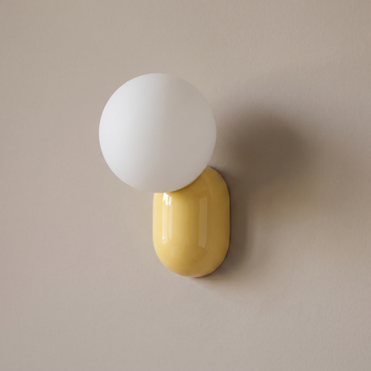 Minimalist macaron yellow resin capsule base and white opal glass globe 1-light wall sconce mounted on a plain greige plaster wall, lamp off