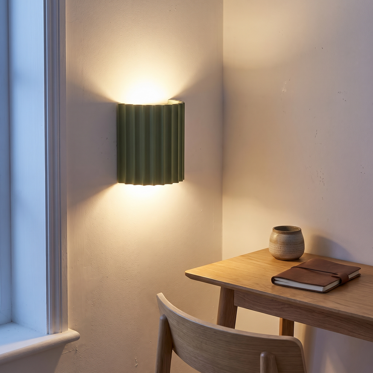 Green striped resin wall sconce lit at dusk above an oak study desk, showing up-and-down light and mounting height