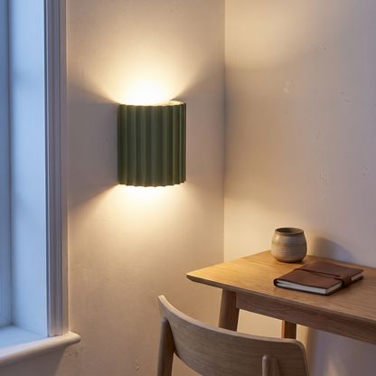 Green striped resin wall sconce lit at dusk above an oak study desk, showing up-and-down light and mounting height