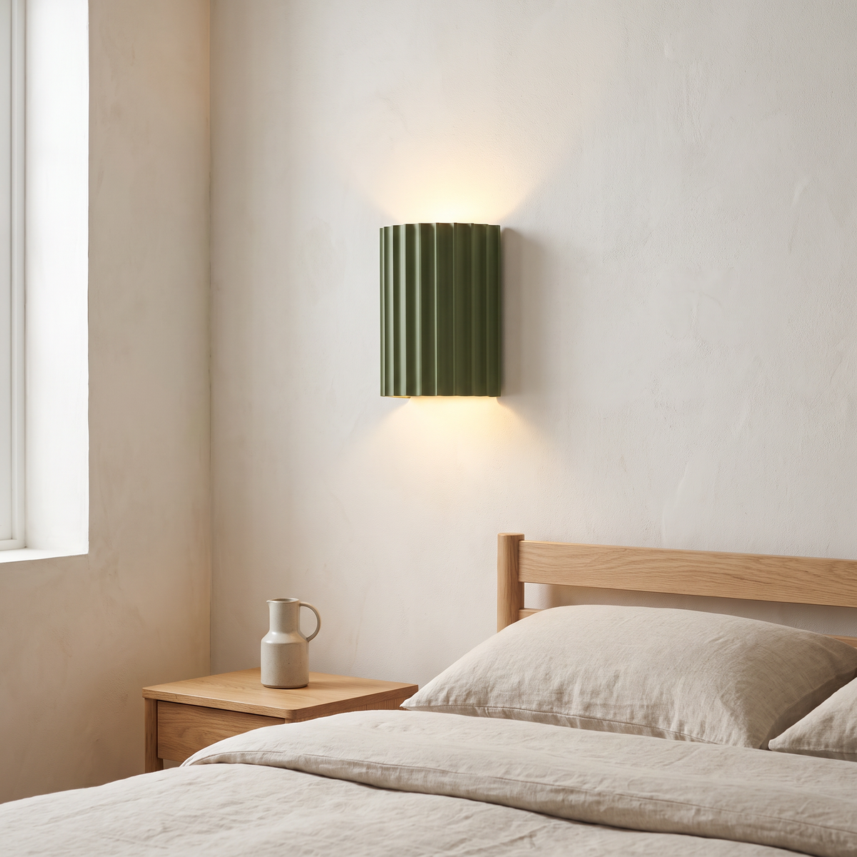 Macaron sage green striped resin half cylinder wall sconce glowing warm up and down the wall above an oak nightstand in a Scandinavian bedroom