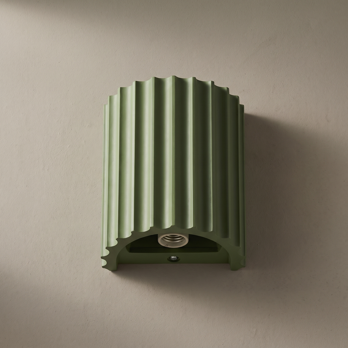 Macaron green fluted resin half cylinder 1-light wall sconce mounted on a plain greige plaster wall, lamp off, showing ribbed texture and G9 socket
