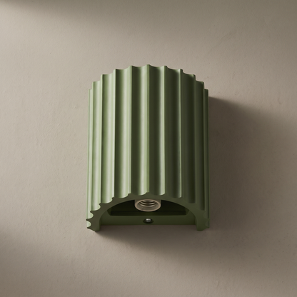Macaron green fluted resin half cylinder 1-light wall sconce mounted on a plain greige plaster wall, lamp off, showing ribbed texture and G9 socket