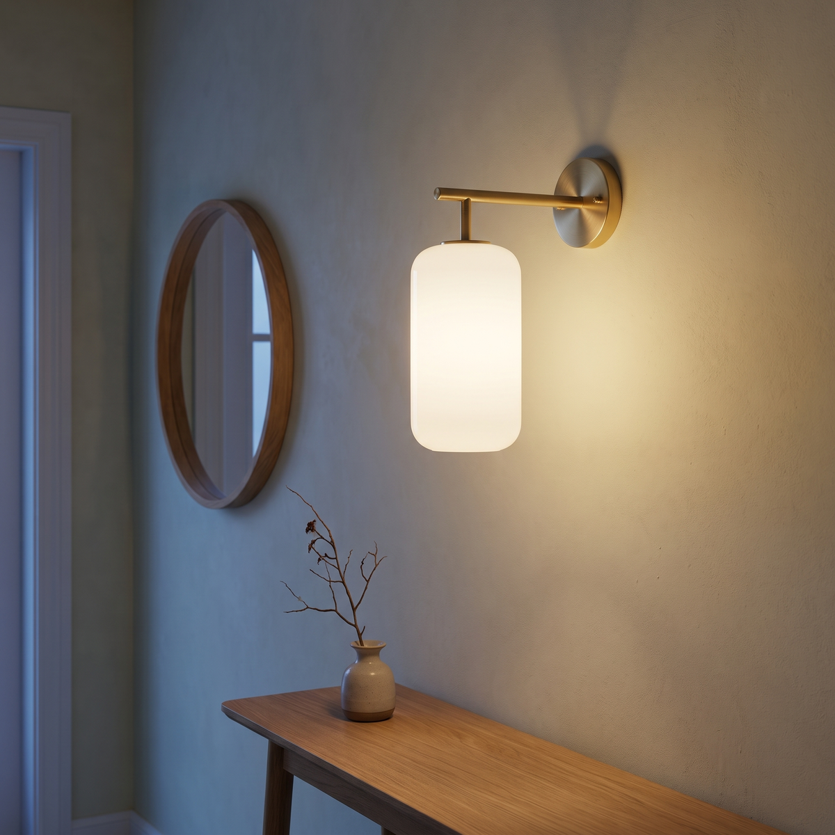 Brass and lucite cylinder wall sconce lit at dusk in a Japandi entry hallway beside an oak console and round mirror, showing 15 cm arm projection and mounting height