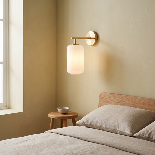 Japanese retro brass and white lucite cylinder wall sconce glowing warm beside a low oak bed in a Japandi lime-washed plaster bedroom