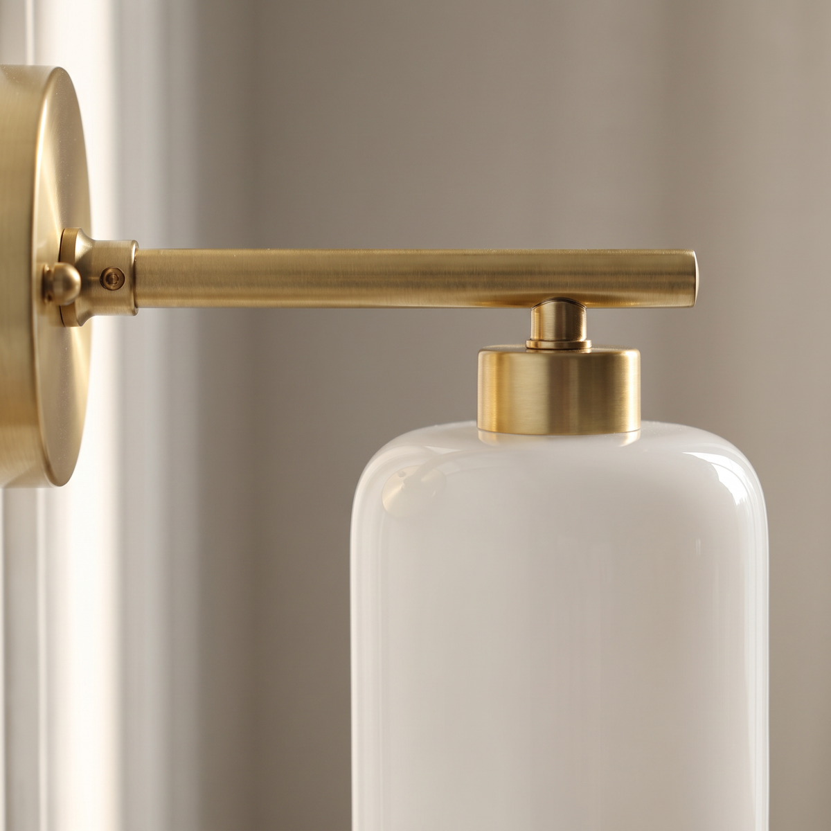 Close-up of the brushed brass round backplate, straight arm and top cap holding the white lucite cylinder shade of the Japanese retro wall sconce