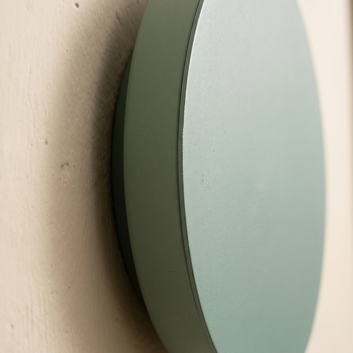 Close-up detail of the matte sage green painted iron edge of the round LED wall sconce and its shadow gap against the wall