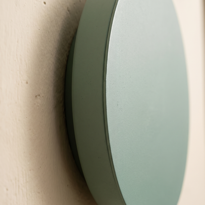 Close-up detail of the matte sage green painted iron edge of the round LED wall sconce and its shadow gap against the wall