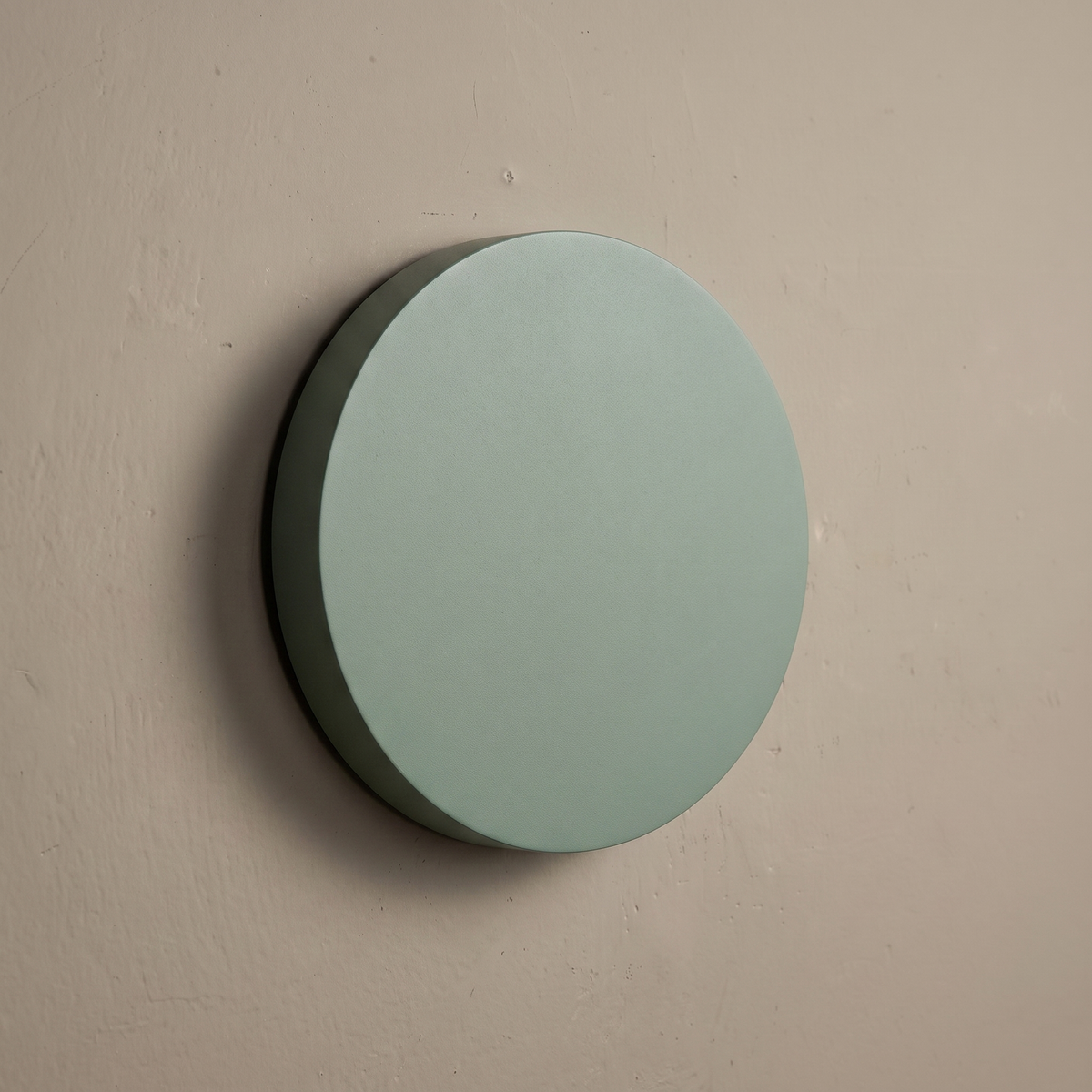 Sage green round iron disc wall sconce mounted on a plain greige plaster wall, lamp off, showing matte finish and slim profile