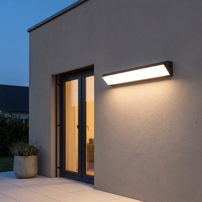 Modern black aluminum acrylic waterproof long LED outdoor wall sconce glowing warm above a patio door on a stucco wall at dusk