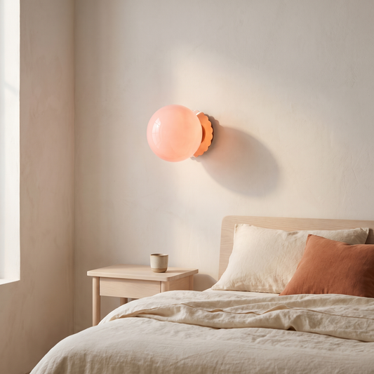 Modern vintage pink glass globe wall sconce with copper backplate glowing warm above a pale ash nightstand in a Scandinavian bedroom